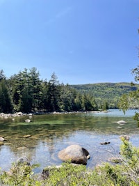 a lake surrounded by rocks and trees on a sunny day